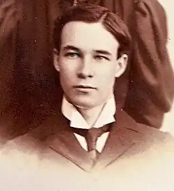 A black and white sepia-toned portrait photograph of a young man in a suit