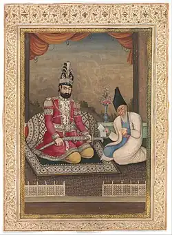 Illustration of two men. To the left is a bearded monarch wearing his full royal costume and crown seated on a raised seat, to the right is a bearded old man seated on the carpet wearing a long cap