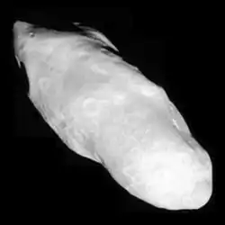 An irregularly shaped oblong body is fully illuminated. It is elongated in the direction from the top left to bottom left. Its surface is covered by craters.