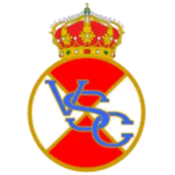 Real Vigo Sporting Club crest, a red and white circle. On the stripe in blue with gold outline are the letters "VSC". A crown sits at the top and the shield has a gold outline.