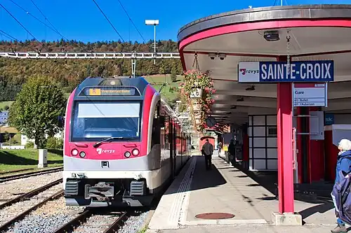 Pink train next to a station sign and shelter