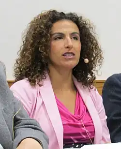 Image of a woman in a pink blouse with curly hair and a head mic