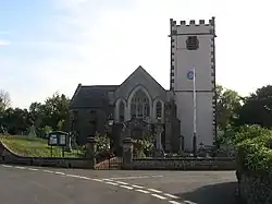 Stone building with white painted square tower. In the foreground is a road junction.