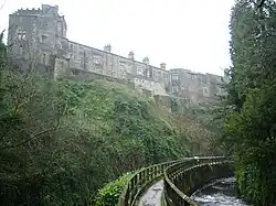 A two- and three-storey building on top of an escarpment. Below the escarpment is a fenced footpath curving away from the photographer's perspective to the right.