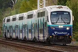 A train with five double-decker passenger cars seen on the furthest of two tracks.