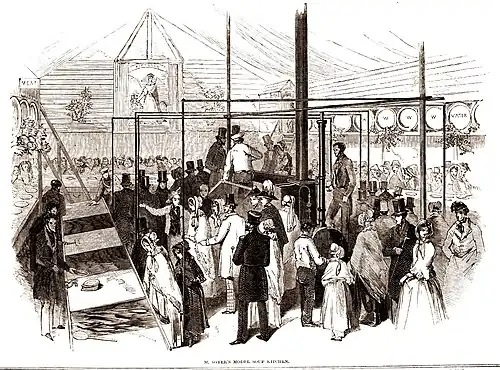 Interior of temporary building with large boiler in them middle and stores and serving stations at each side. The space is full of the great and good in smart clothes for the official opening ceremony