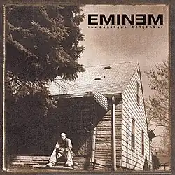 A sepia toned image of Eminem sitting in front of an old house and a tree covering part of the house. On the top right is the "EMINEM" logotype with"the marshall mathers lp" immediately below it in a smaller font