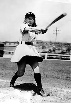 A female baseball player wearing a dress-like uniform, swingin her bat.