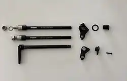Three M12 through-axles: Top: 1 mm pitch axle for bicycle trailer (via M10 bolt) with spacers for adjustable axle length (160-178 mm), 37 mm thread length, shown with a universal derailleur hanger (UDH). Bottom: 1.5 mm pitch axle with tool-less handle, without M10 nut and hence not suitable for attaching a bicycle trailer