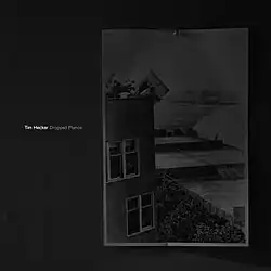 A picture is pinned to a wall depicting a piano getting thrown off a roof. The artist's name and release's name is beside the picture.