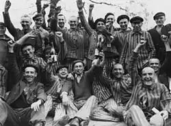 Dachau survivors toast their liberation as the man standing in center between the bottles wears a P triangle.