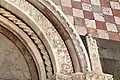 Medallions from right superior frieze of portal, depicting showing veneration of the crucifixion, and education of students; an Archangel flanks the portal