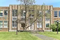 An old two-story school front with a large tree in the foreground