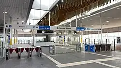 Interior of a train station, with fare gates and stairs down to the platform below