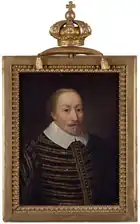 A balding man with a grey and blond goatee with a large white collar and a striped gold and black tunic