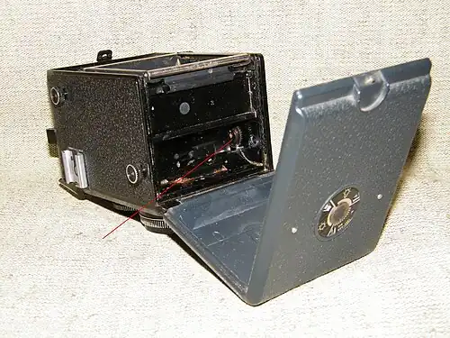 Стрелкой указан зубчатый ролик, отслеживающий сантиметры перематываемой фотоплёнки. На задней стенке - шкала-памятка типа фотоплёнки и её светочувствительности.