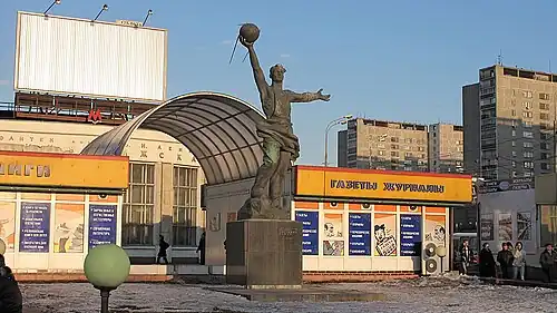 Памятник на фоне павильона печатной продукции, простоявшего до обустройства территории у станции метро «Рижская» в 2015 году.Апрель 2009 г.