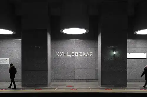 Колонны, потолочные светильники и стена с названием станции, вид сбоку