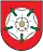A coat of arms depicting a white flower in the middle that has a yellow stamen and green leaves all on a red background