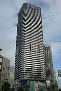 Ground-level view of a white, rectangular high-rise; the corners are cut and balconies form horizontal stripes up the height of the tower