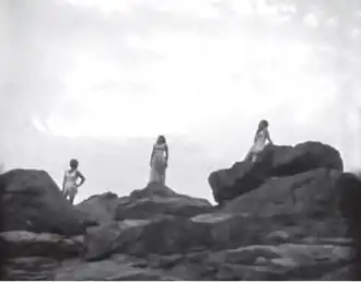 Женщины неподвижно стоят на скалистом прибрежном утёсе. Финальная сцена фильма.