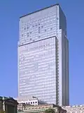 Ground-level view of a rectangular, glass high-rise; adjoining the high-rise is a stone building featuring columns