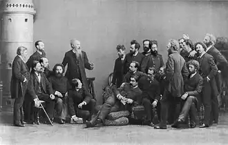 Фотография группы членов ТПХВ (1888 г.). Стоят: (слева направо) — А. К. Беггров, Н. Н. Дубовской, И. И. Шишкин, В. М. Максимов, П. А. Брюллов, Л. В. Позен, Н. А. Ярошенко, К. А. Савицкий, Н. В. Неврев, В. Е. Маковский, И. Е. Репин, Г. Г. Мясоедов. Сидят (слева направо) — А. А. Киселёв, Е. Е. Волков, А. И. Куинджи, А. М. Васнецов, Н. Д. Кузнецов, К. В. Лемох, М. П. Клодт, И. М. Прянишников, Н. К. Бодаревский