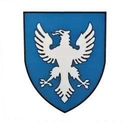 На синем щите изображён белый орёл, в позе крыльями вверх, снизу с расставленными лапами и нижнем опереньем хвоста, смотрящий в левую сторону