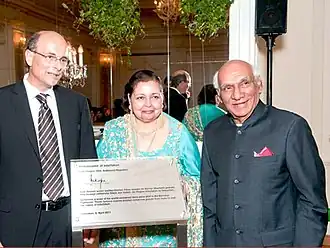 Представитель Швейцарии вручает Памеле и Яшу Чопре наградной сертификат